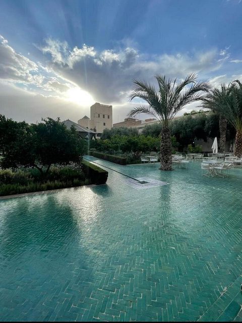 The wide green zellige pool at sunset, palms and terrace